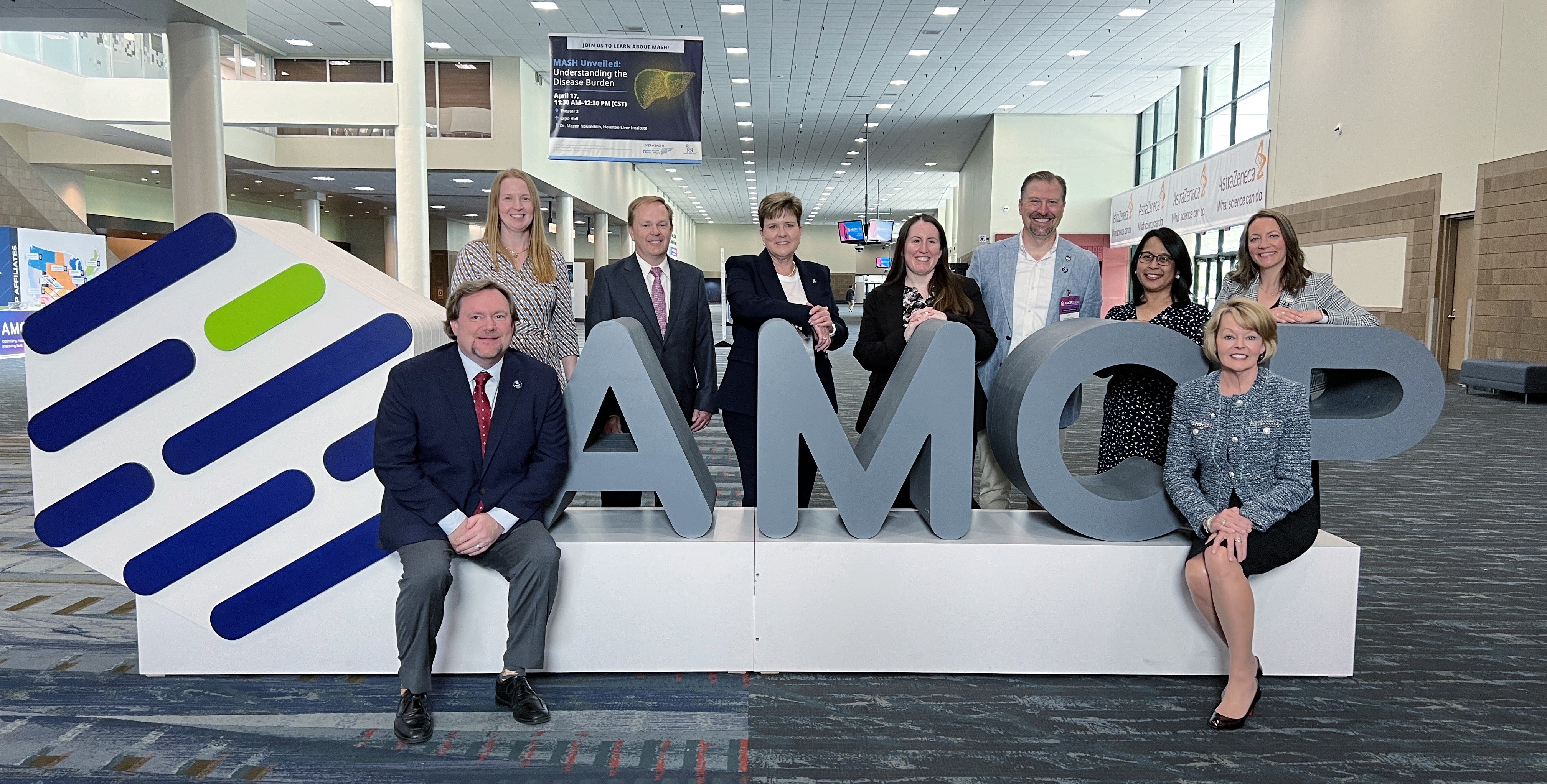 Ten people posing for a photo next to a large AMCP logo.